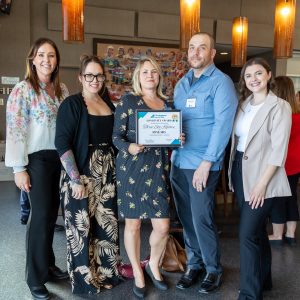 A group of professionals holding a framed recognition at a business event.