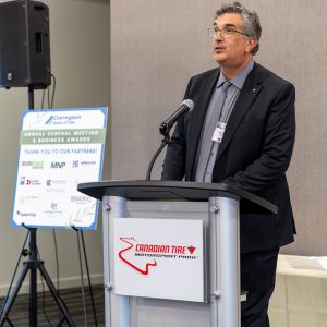A professional man delivering speech at Clarington Board of Trade annual meeting, behind a podium at Canadian Tire Motorsport Park.