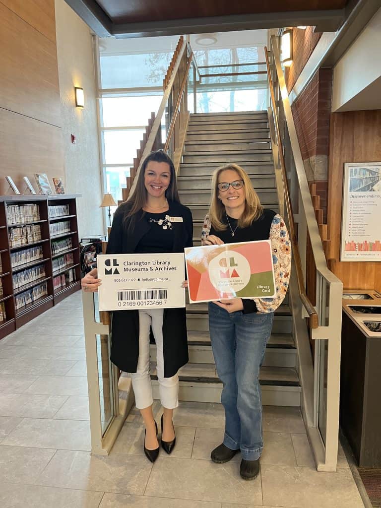 Two women holding Clarington Library partnership signs inside a library.