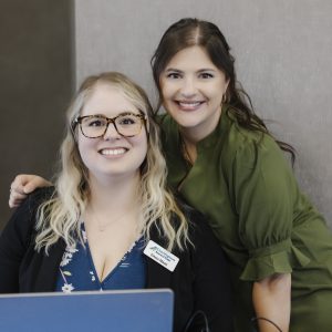 Two women smiling at a Clarington Board of Trade event, with a laptop and networking equipment.